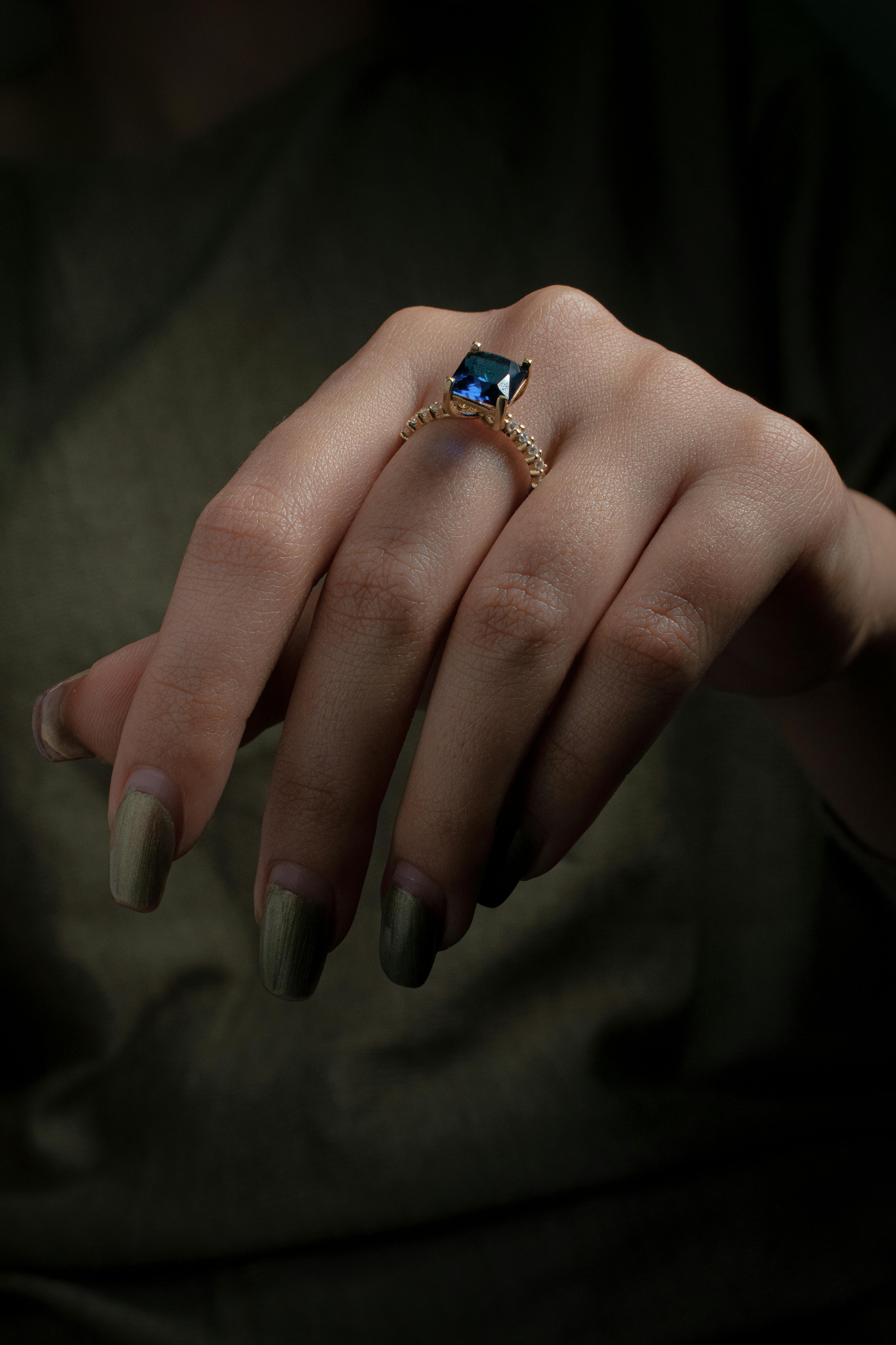 Sapphire ring on hand with green nails, green fabric background