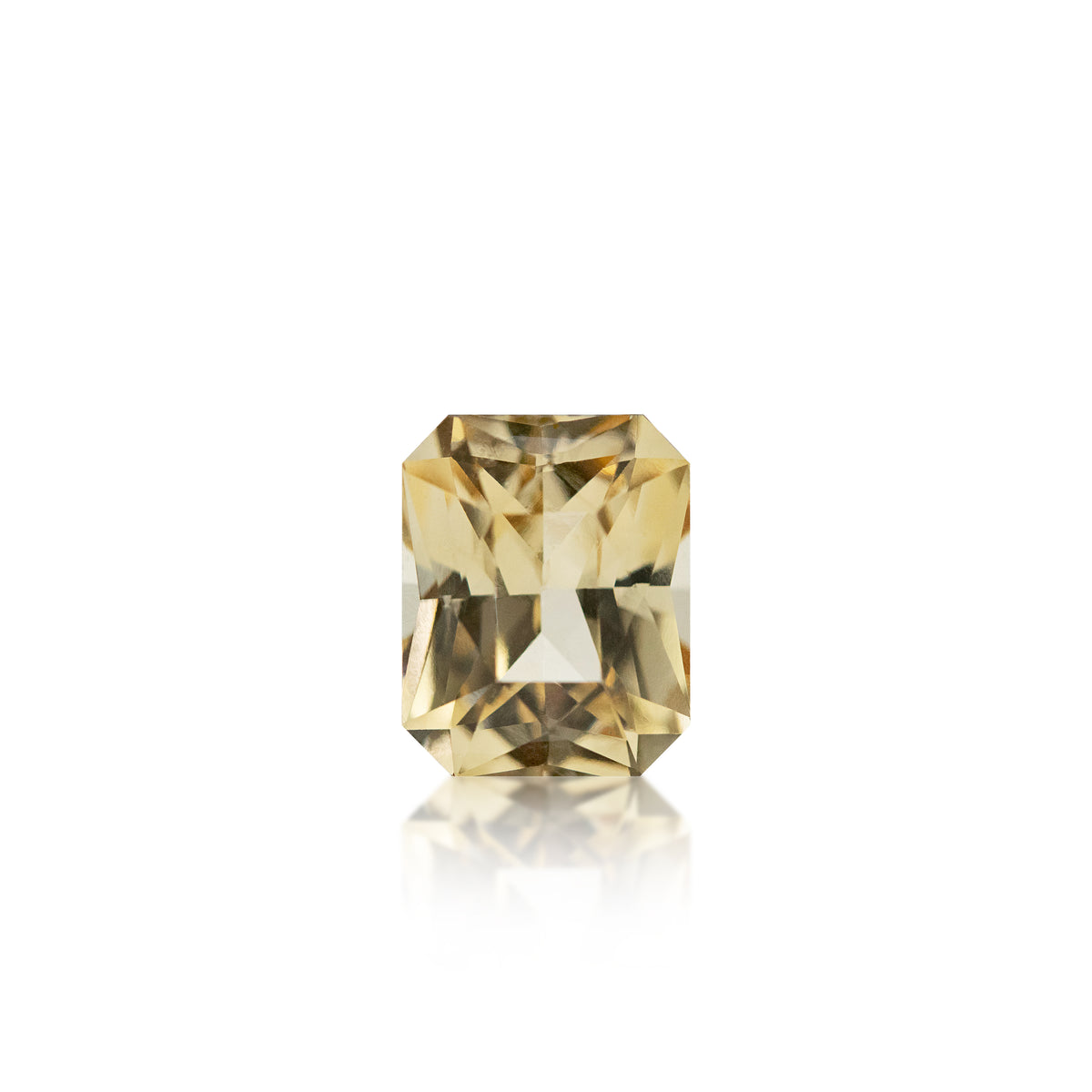 A single rectangular emerald-cut yellow gemstone with a warm golden-brown hue, centered on a clean white background with a soft reflection below.