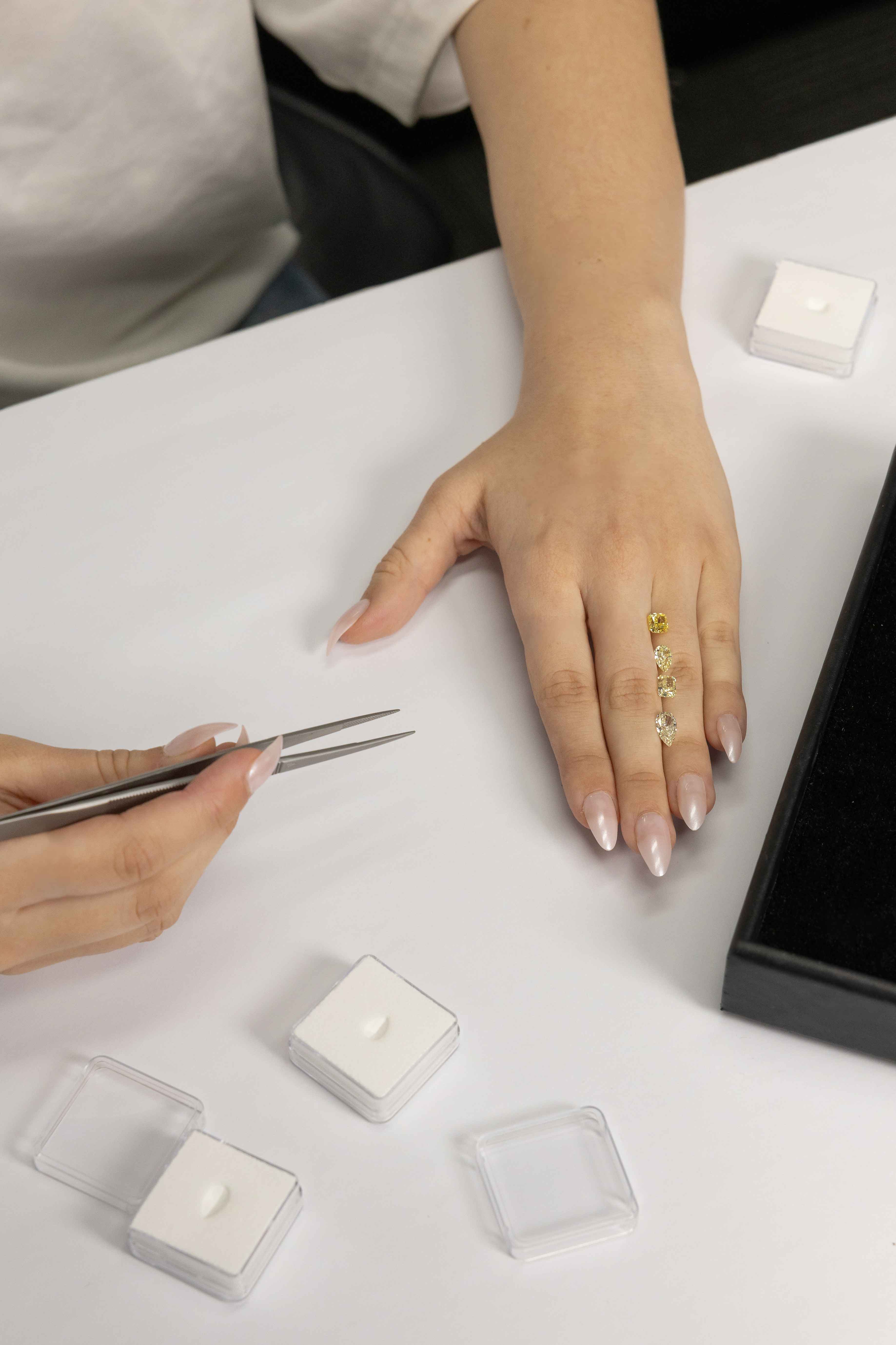 Person positioning yellow diamonds on a hand on a white surface with small clear containers.