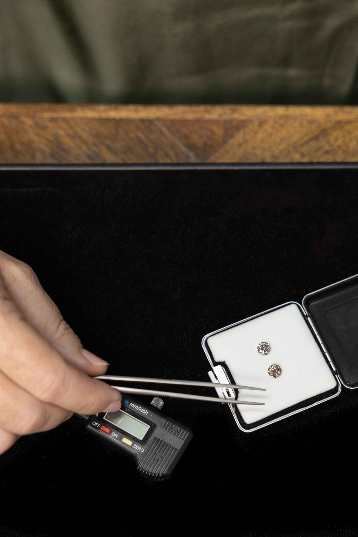 Person using tweezers to handle a diamond in a jewelry box on a black surface.