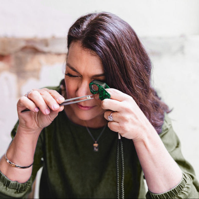 Woman examining a green gemstone with tweezers