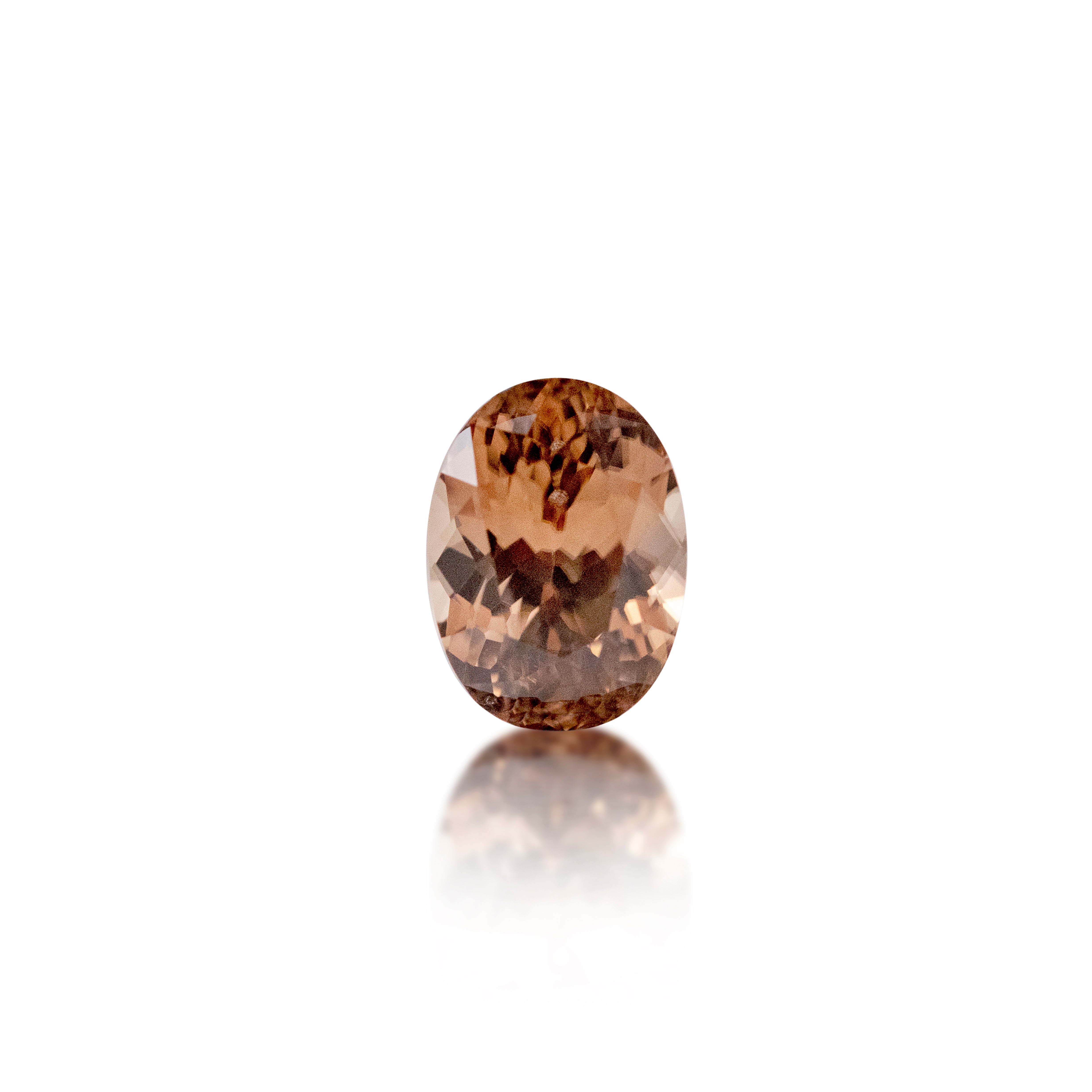 An oval-cut faceted gemstone in a warm peachy-brown color, centered on a clean white background with a soft reflection below.
