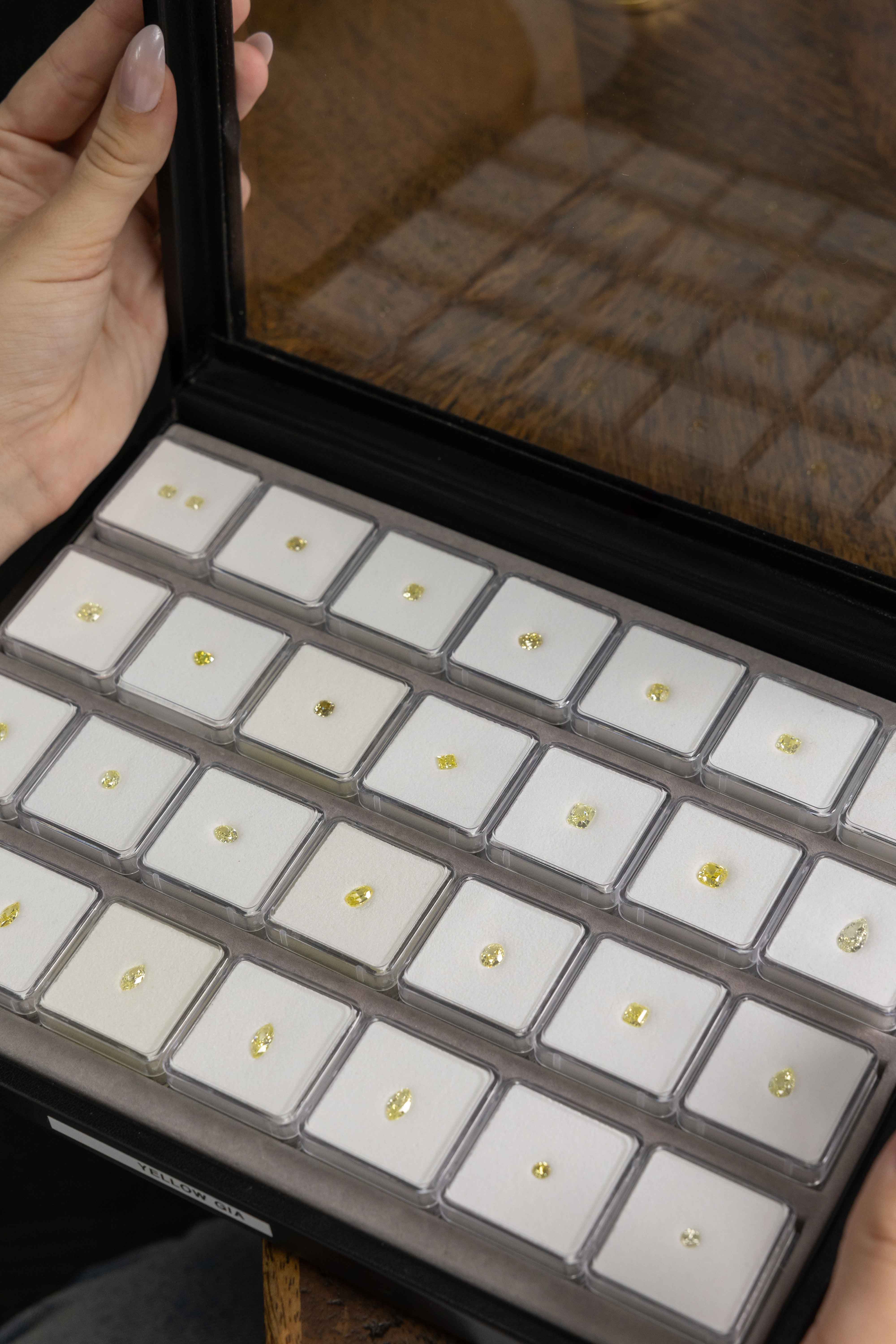 Tray of yellow diamonds, variety of shapes, in a clear case held by a person.