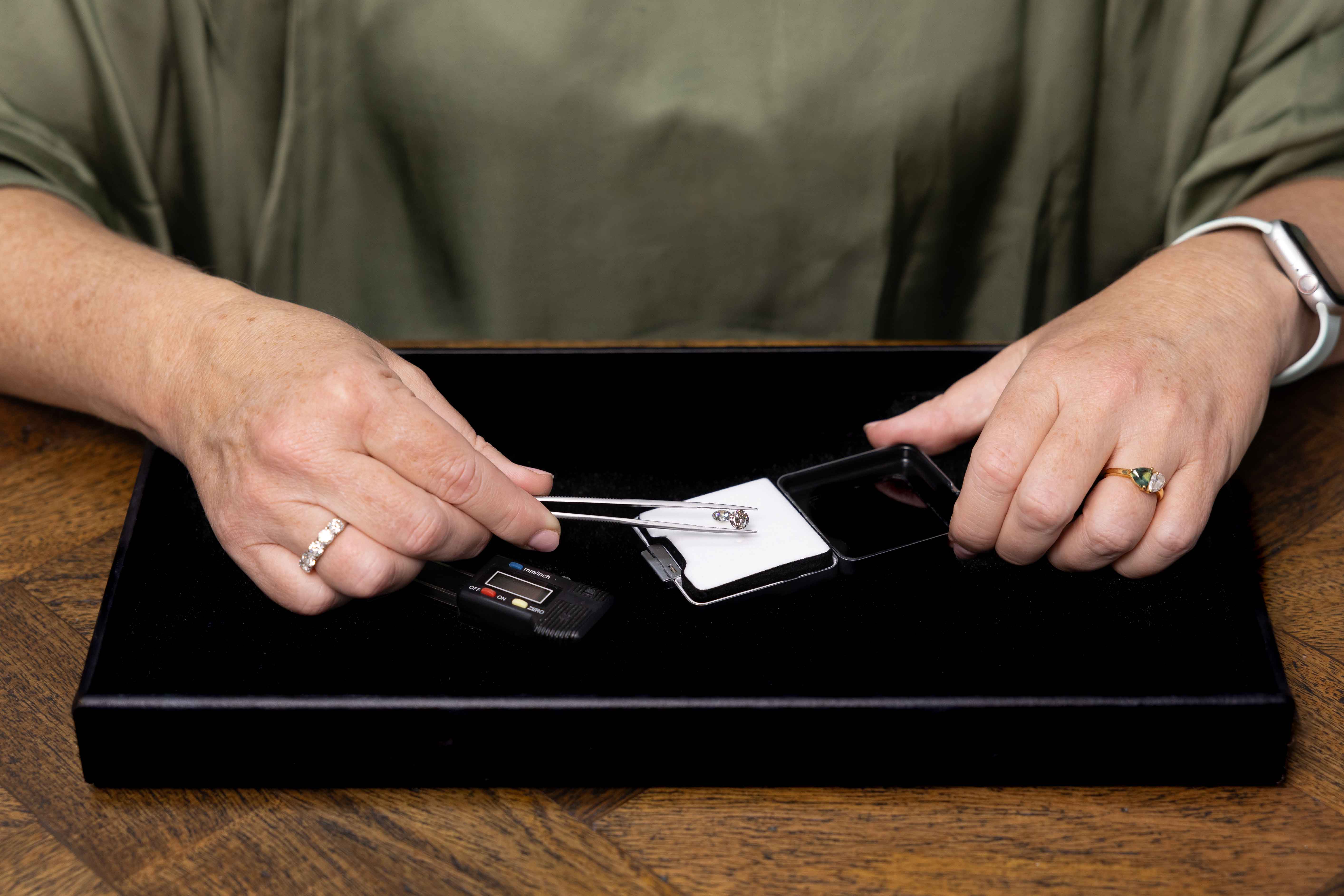 Person handling small electronic devices on a black tray with a wooden surface. Holding a diamond.